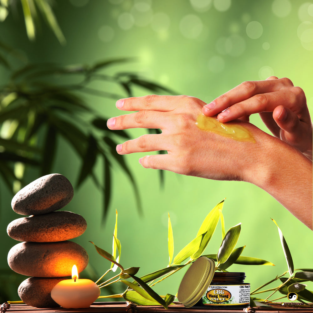 A women rubbing rubbing topical salve on to her hands with an open salve jar. A candle, some rocks, and a green background with bamboo.